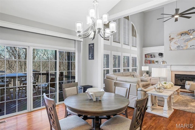 997 Sheffield Forest Ct, Wildwood, MO 63021 - dining space featuring wood finished floors, healthy amount of natural light, high vaulted ceiling, a chandelier, and a glass covered fireplace