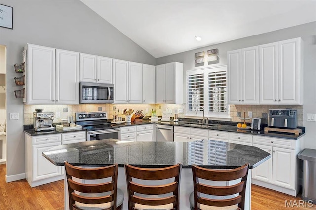 997 Sheffield Forest Ct, Wildwood, MO 63021 - kitchen with appliances with stainless steel finishes, a sink, white cabinetry, vaulted ceiling, and a breakfast bar