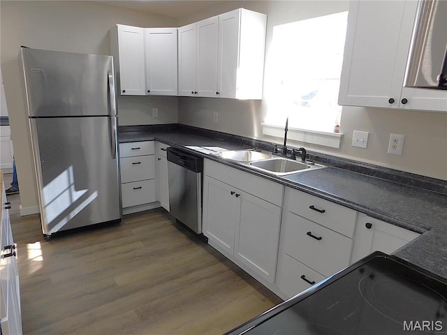 kitchen with appliances with stainless steel finishes, a sink, dark countertops, wood finished floors, and white cabinetry