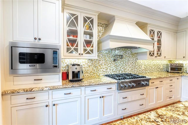 16 Holiday Ln, Saint Louis, MO 63131 - kitchen with stainless steel appliances, custom exhaust hood, decorative backsplash, glass insert cabinets, and white cabinets