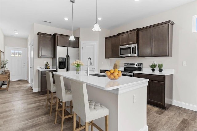 kitchen with appliances with stainless steel finishes, a sink, dark brown cabinetry, light wood finished floors, and baseboards