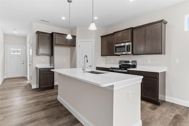 kitchen featuring stainless steel appliances, a sink, dark brown cabinets, baseboards, and wood finished floors