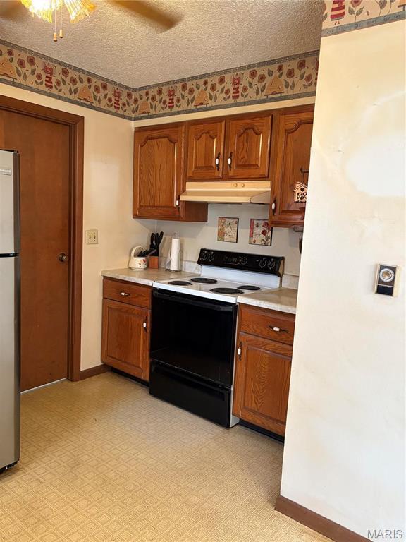 10019 Seabourne St, Belgrade, MO 63622 - kitchen with electric stove, under cabinet range hood, freestanding refrigerator, light countertops, and brown cabinets