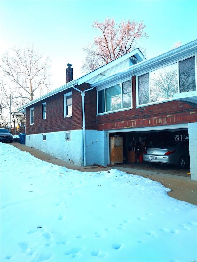 2106 Lackland Rd, Saint Louis, MO 63114 - snow covered property with a chimney, an attached garage, brick siding, and asphalt driveway