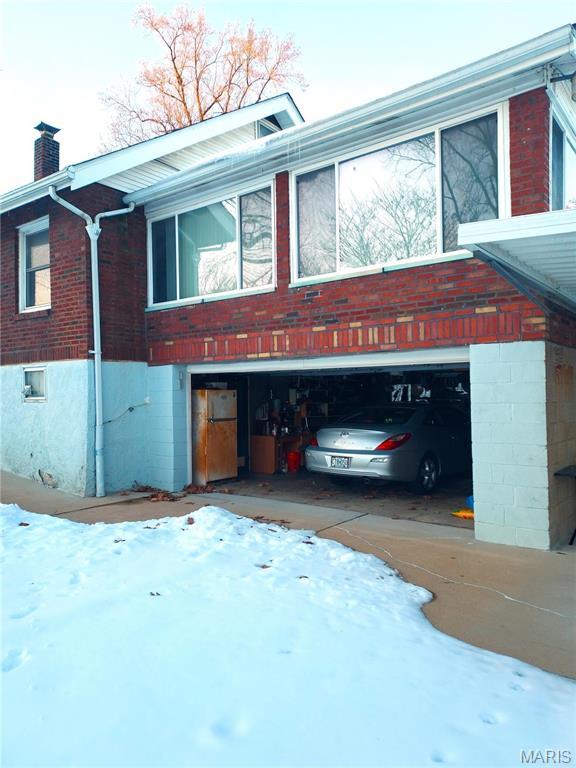 2106 Lackland Rd, Saint Louis, MO 63114 - snow covered property featuring a chimney, a garage, and brick siding