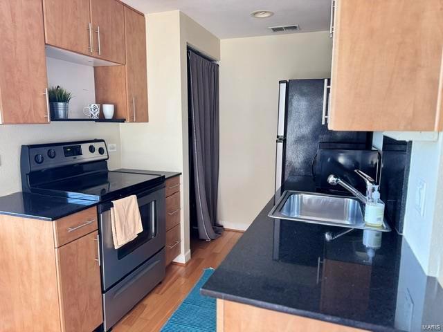 kitchen featuring appliances with stainless steel finishes, a sink, light wood-style flooring, dark countertops, and brown cabinetry
