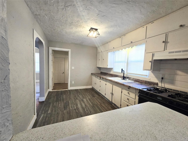 kitchen featuring under cabinet range hood, a sink, black range with gas cooktop, dark wood-style flooring, and baseboards