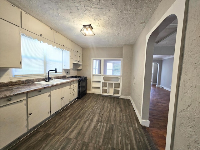 kitchen with black range with gas cooktop, arched walkways, a sink, dark wood-style floors, and under cabinet range hood