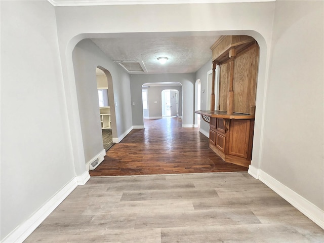 hallway with arched walkways, wood finished floors, and baseboards