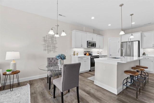 kitchen featuring appliances with stainless steel finishes, a sink, wood finished floors, a kitchen island with sink, and recessed lighting