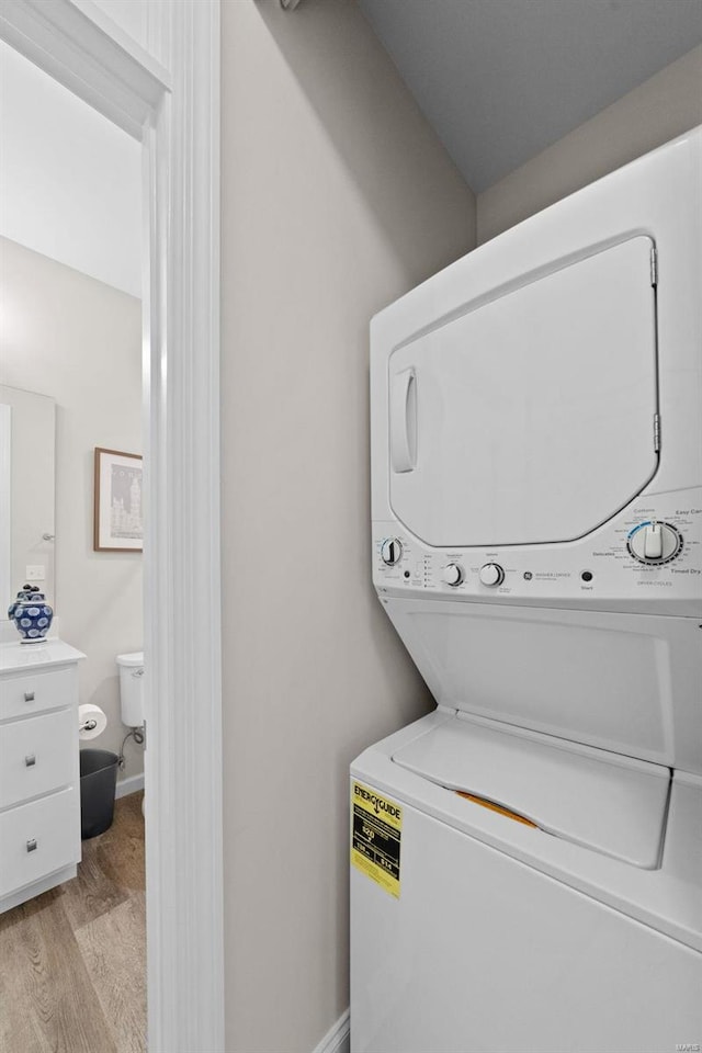 clothes washing area featuring stacked washer / dryer, light wood-style floors, and baseboards