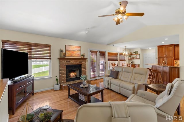 living area featuring lofted ceiling, ceiling fan, a chandelier, a brick fireplace, and light wood finished floors