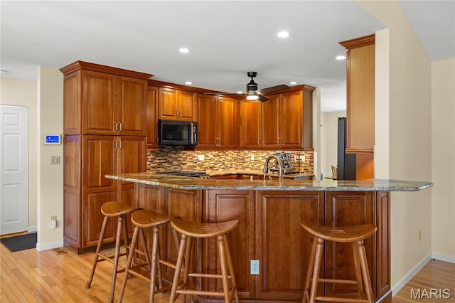 kitchen featuring dark stone countertops, a ceiling fan, backsplash, a peninsula, and light wood finished floors