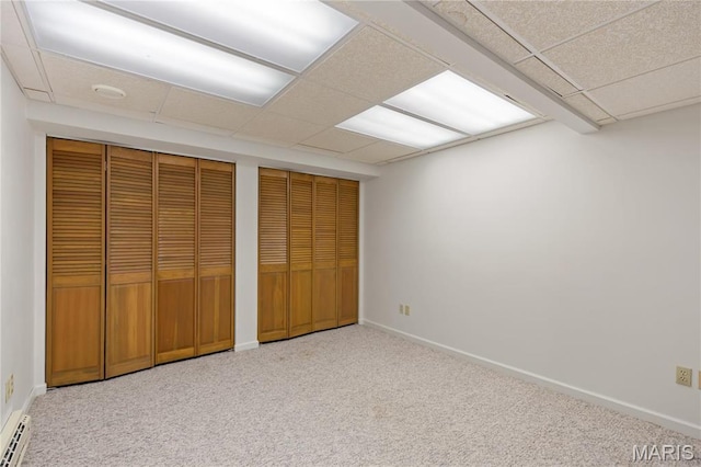 unfurnished bedroom with multiple closets, a drop ceiling, carpet floors, and baseboards