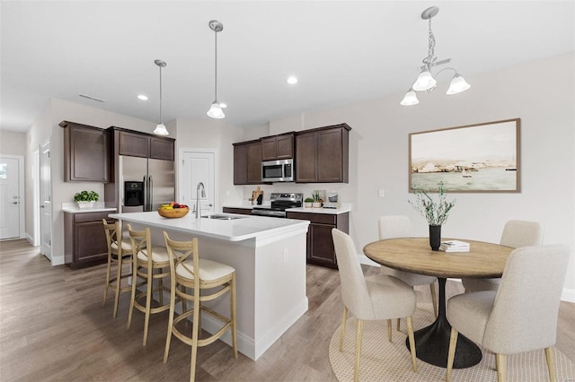 kitchen with stainless steel appliances, light wood finished floors, a sink, dark brown cabinetry, and baseboards