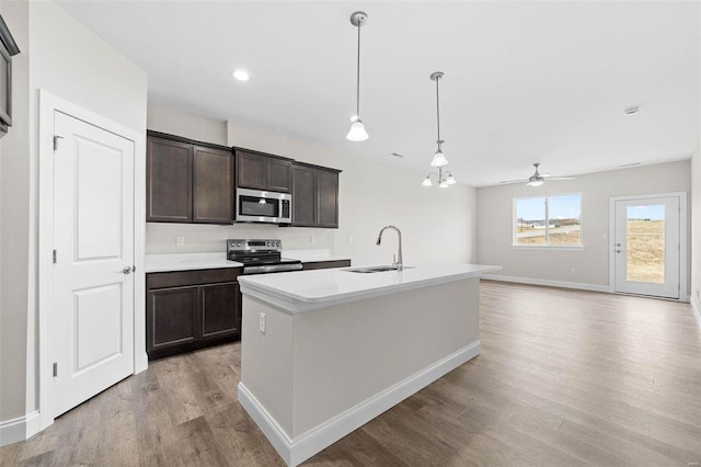 kitchen featuring stainless steel appliances, a sink, light wood finished floors, dark brown cabinets, and baseboards