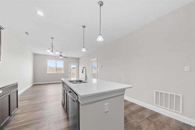 kitchen with stainless steel dishwasher, a sink, wood finished floors, light countertops, and an island with sink