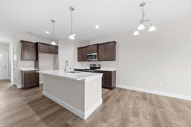 kitchen with stainless steel appliances, light wood-style floors, a sink, dark brown cabinets, and baseboards