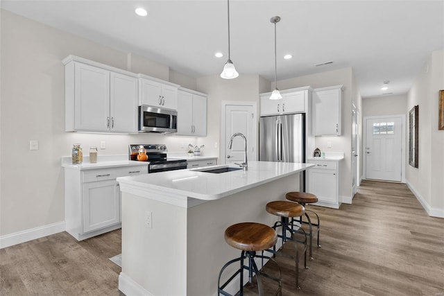 kitchen with appliances with stainless steel finishes, a sink, wood finished floors, a kitchen bar, and baseboards