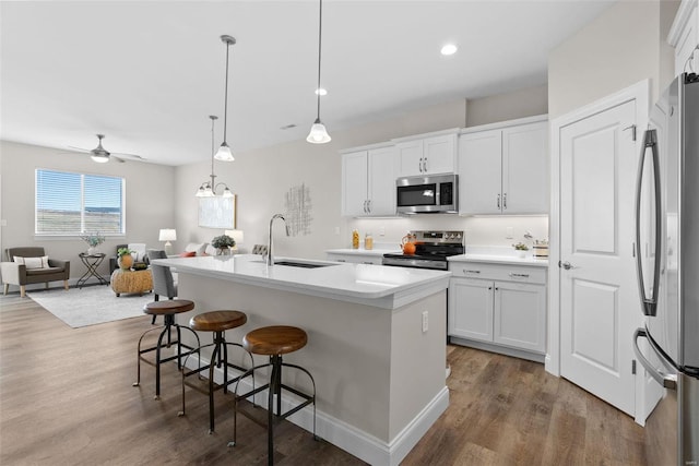 kitchen featuring stainless steel appliances, open floor plan, a sink, wood finished floors, and a kitchen bar