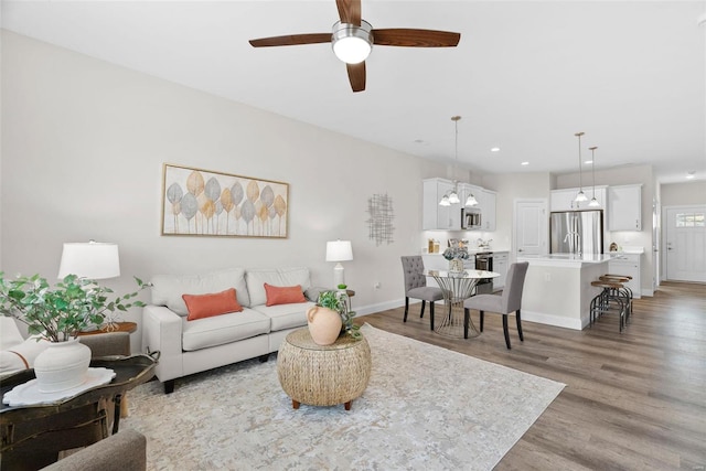 living area featuring light wood-style floors, recessed lighting, ceiling fan, baseboards, and a chandelier