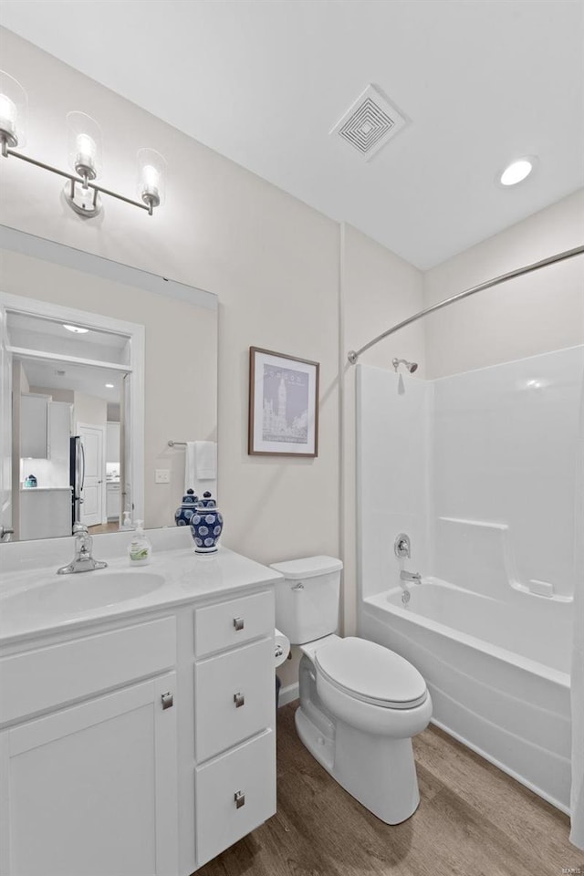 bathroom with wood finished floors, toilet, vanity, bathing tub / shower combination, and baseboards