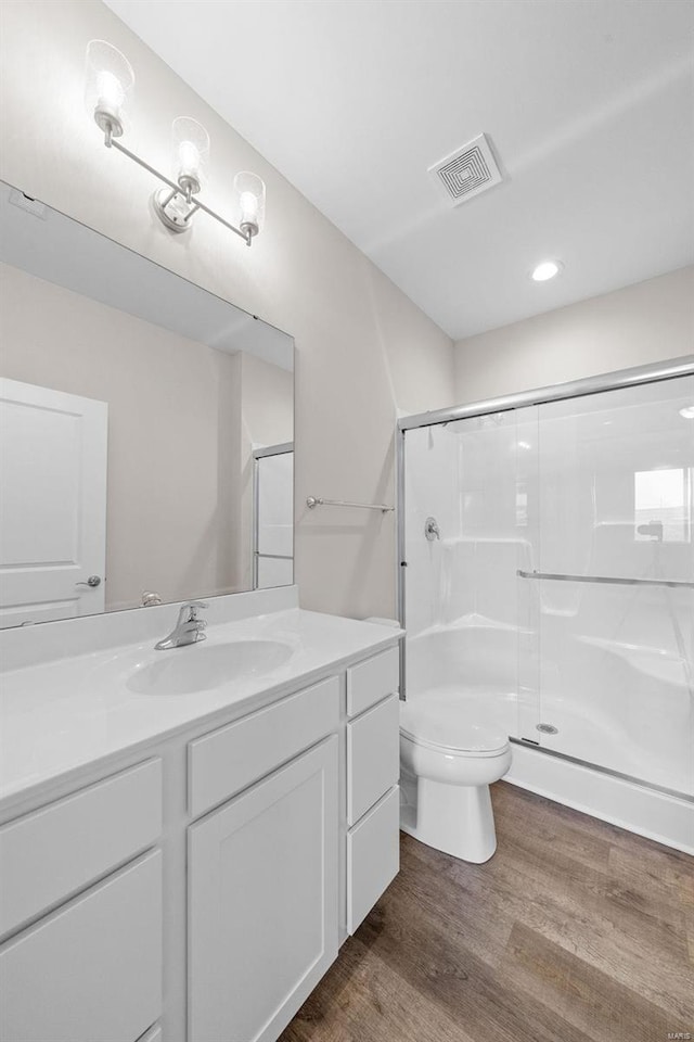 bathroom with toilet, a stall shower, wood finished floors, vanity, and recessed lighting