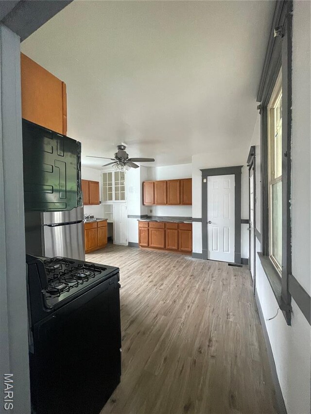 4947 Rosalie St, Saint Louis, MO 63115 - kitchen featuring black range with gas stovetop, light wood-style floors, brown cabinetry, a ceiling fan, and fridge