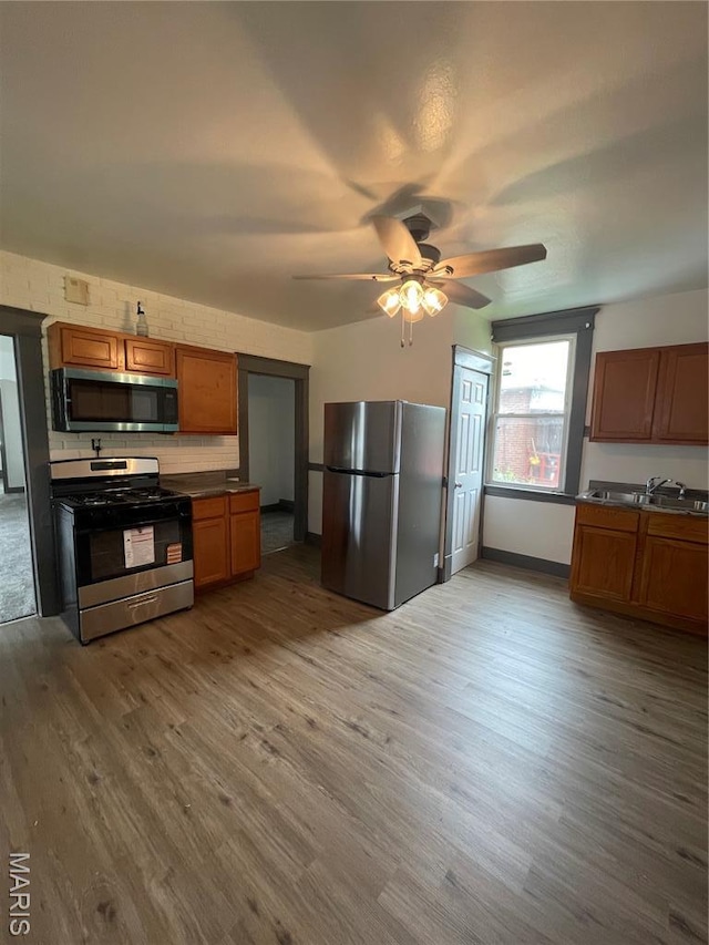4947 Rosalie St, Saint Louis, MO 63115 - kitchen with stainless steel appliances, wood finished floors, a ceiling fan, a sink, and brown cabinetry