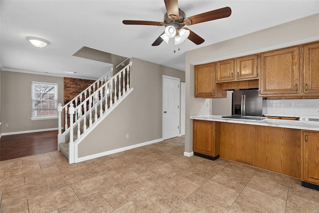kitchen with stainless steel refrigerator with ice dispenser, brown cabinets, baseboards, and ceiling fan