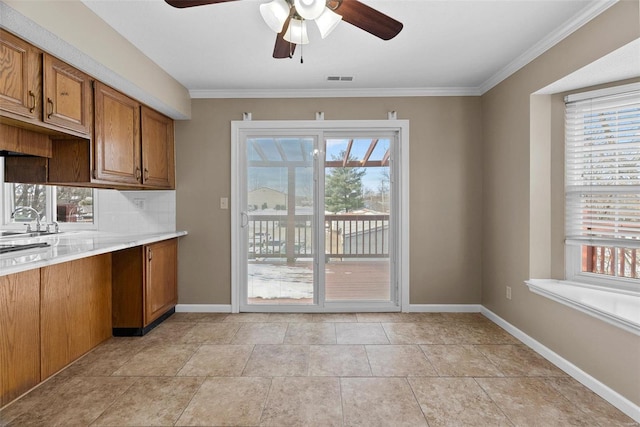 kitchen with plenty of natural light, brown cabinets, a ceiling fan, light countertops, and ornamental molding