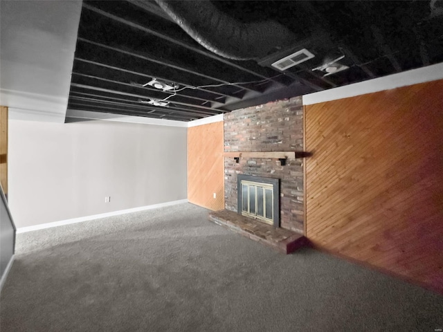 unfurnished living room with carpet, a fireplace, wood walls, and baseboards