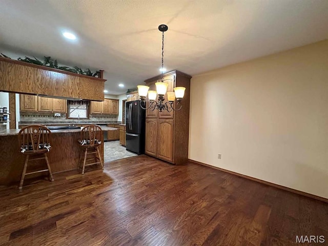 17264 Cedar Hills Dr, Dexter, MO 63841 - kitchen with freestanding refrigerator, a chandelier, dark wood-type flooring, a kitchen breakfast bar, and a peninsula