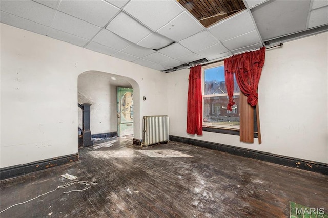 7307 Minnesota Ave, Saint Louis, MO 63111 - empty room with radiator, arched walkways, a paneled ceiling, hardwood / wood-style floors, and baseboards