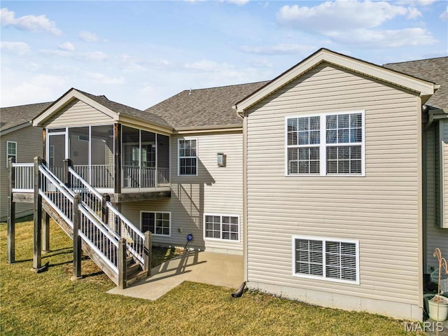 back of property with a sunroom, a patio area, a lawn, and roof with shingles