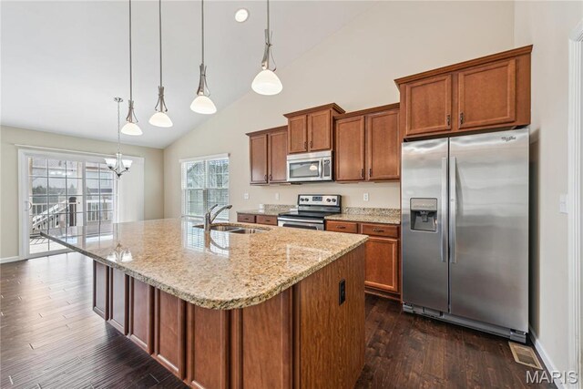kitchen featuring appliances with stainless steel finishes, a sink, brown cabinetry, dark wood-style flooring, and a kitchen island with sink