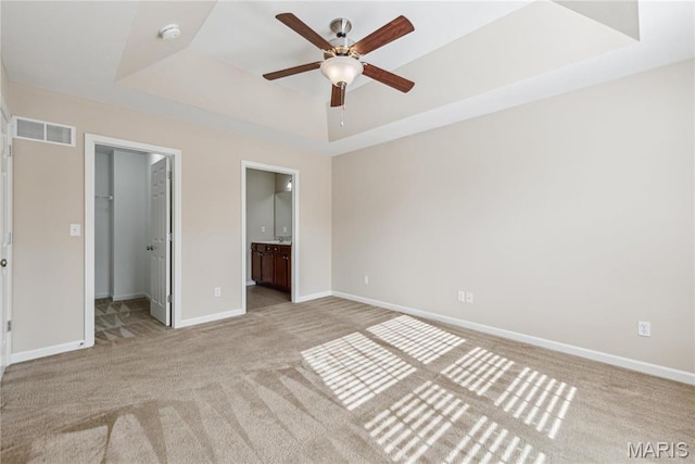 unfurnished bedroom with a tray ceiling, light carpet, a spacious closet, baseboards, and connected bathroom