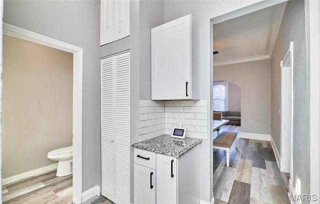 2922 S Compton Ave, Saint Louis, MO 63118 - kitchen with light stone countertops, arched walkways, light wood finished floors, white cabinets, and baseboards