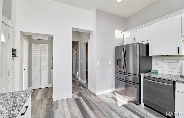2922 S Compton Ave, Saint Louis, MO 63118 - kitchen featuring stainless steel appliances, white cabinets, light stone countertops, light wood-style floors, and tasteful backsplash