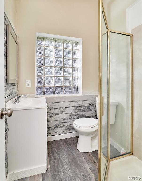 2922 S Compton Ave, Saint Louis, MO 63118 - full bathroom with vanity, a shower stall, wood finished floors, toilet, and a wainscoted wall