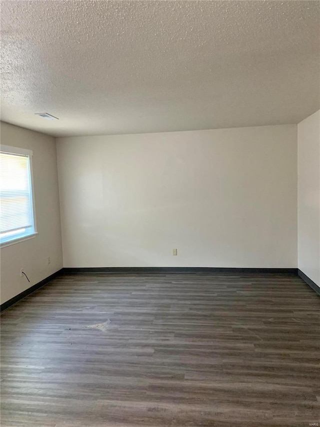 spare room with a textured ceiling, wood finished floors, and baseboards