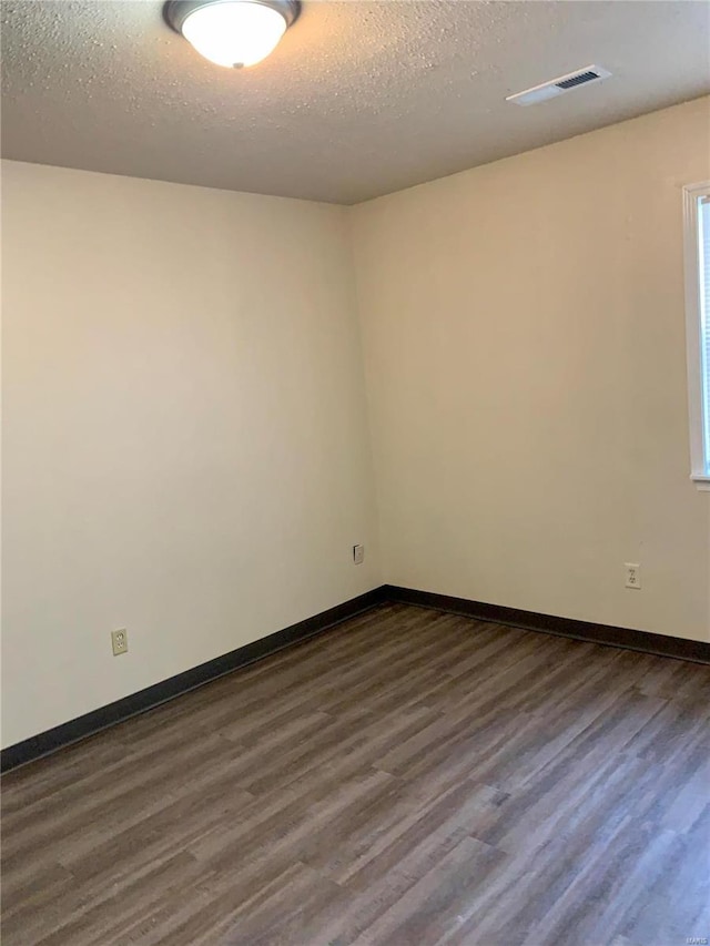 empty room featuring dark wood-type flooring, a textured ceiling, and baseboards