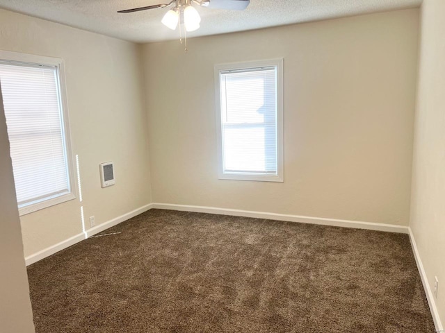 empty room featuring dark carpet, ceiling fan, baseboards, a textured ceiling, and heating unit