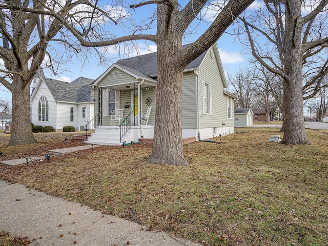view of front facade featuring a porch, roof with shingles, and a front yard