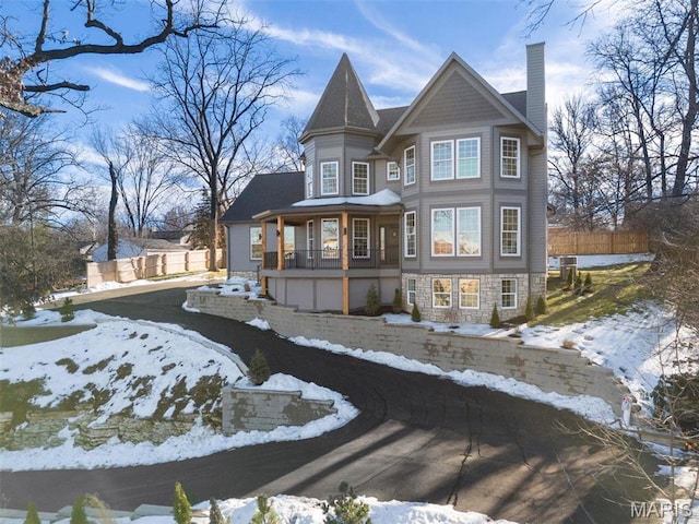 snow covered back of property with a chimney, stone siding, and a porch