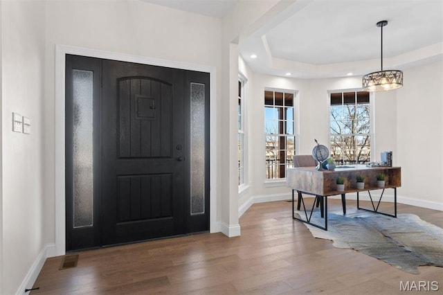 foyer featuring wood finished floors, a chandelier, baseboards, recessed lighting, and a raised ceiling