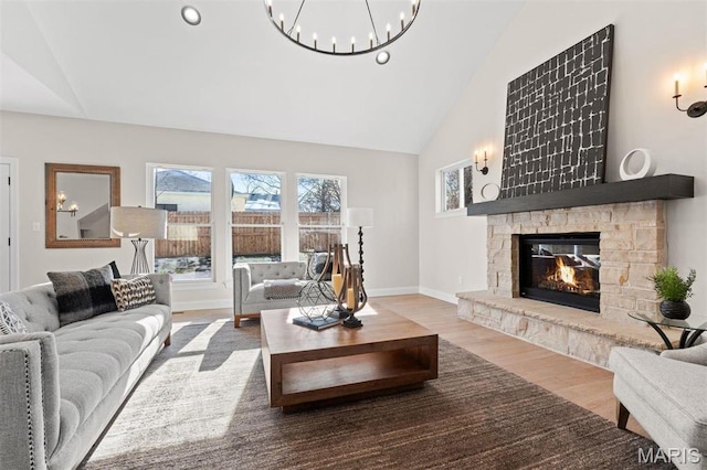 living room with wood finished floors, a stone fireplace, high vaulted ceiling, a chandelier, and baseboards