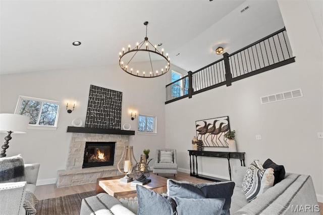 living area with a chandelier, high vaulted ceiling, a stone fireplace, baseboards, and wood finished floors