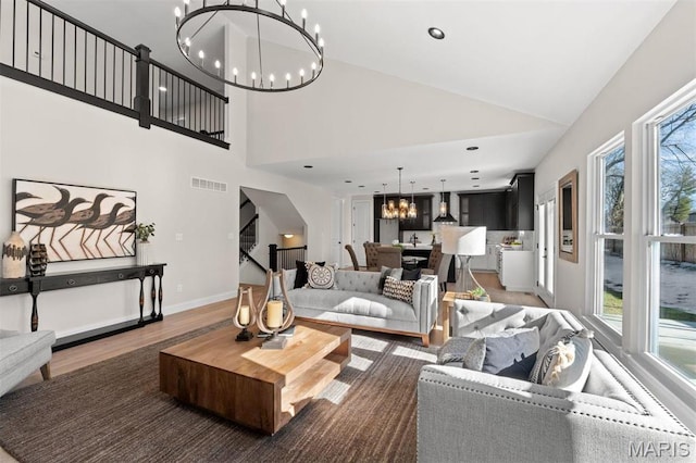 living area featuring a chandelier, plenty of natural light, high vaulted ceiling, wood finished floors, and baseboards