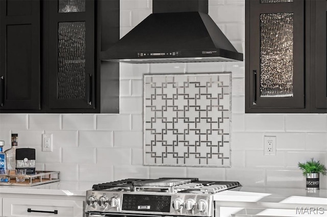 kitchen featuring wall chimney range hood, gas stove, dark cabinets, backsplash, and light countertops